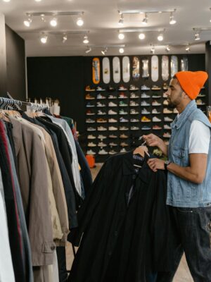 Man in a beanie and denim jacket shopping for coats in a trendy clothing store.