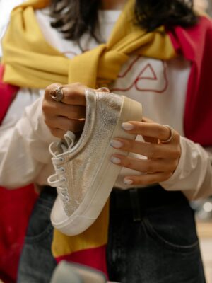 Woman shopping in store holding glittery sneakers. Fashionable retail moment.